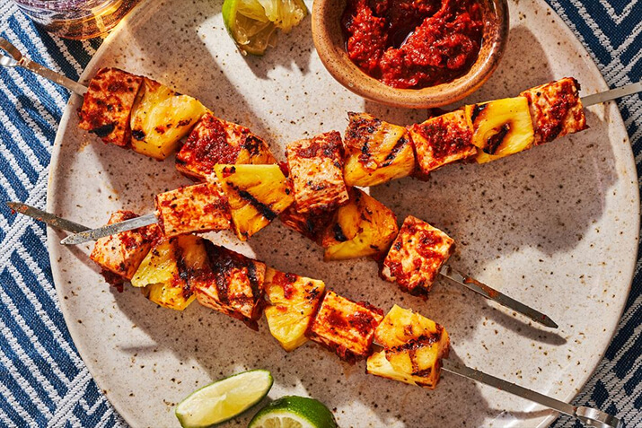 Grilled chipotle tofu and pineapple on skewers with lime wedges.