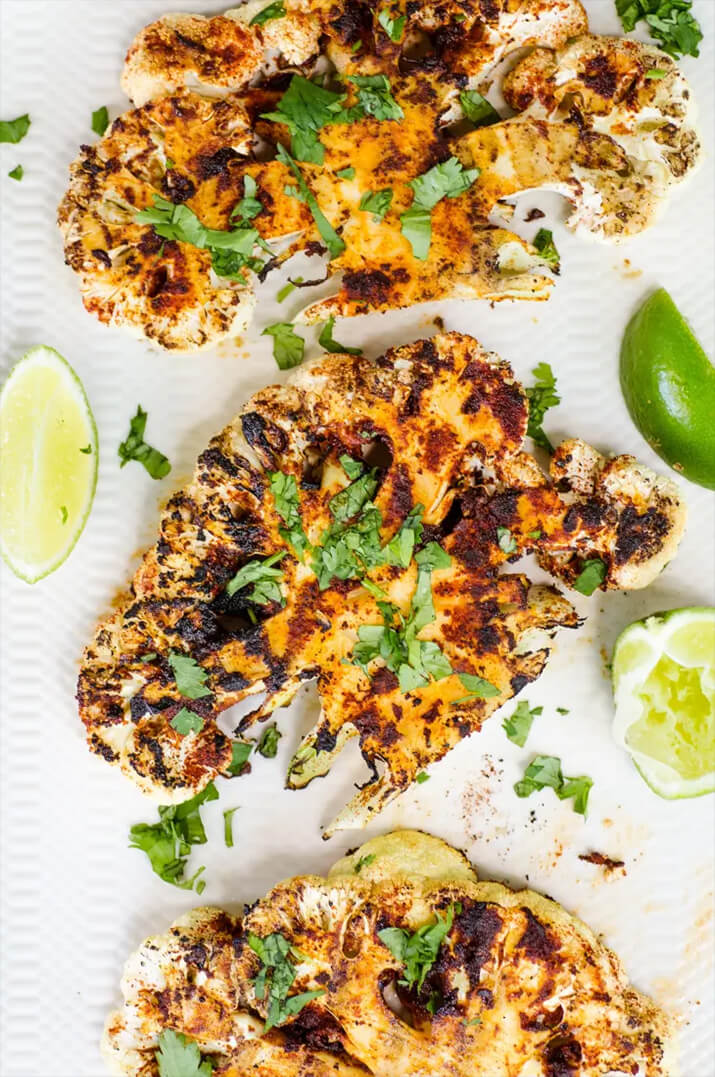 Grilled cauliflower steaks with cilantro and lime wedges.