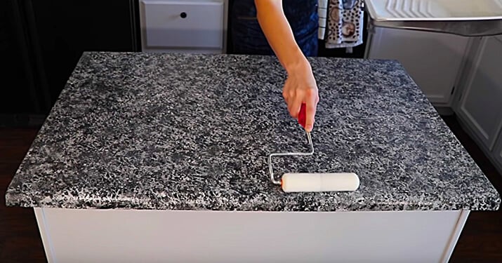 Applying a topcoat to faux granite countertops with a paint roller.