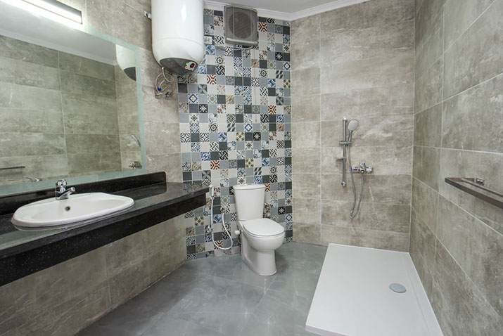 Wet room with patterned accent tile wall, floor-mounted toilet, dark stone countertop vanity, and a curbless shower with wall-mounted fixtures.