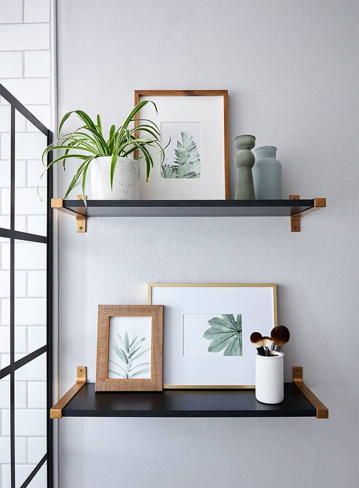 Black floating shelves in bathroom holding art and plants.