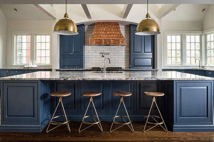 Blue kitchen with gold statement lighting fixtures and subway tile backsplash.