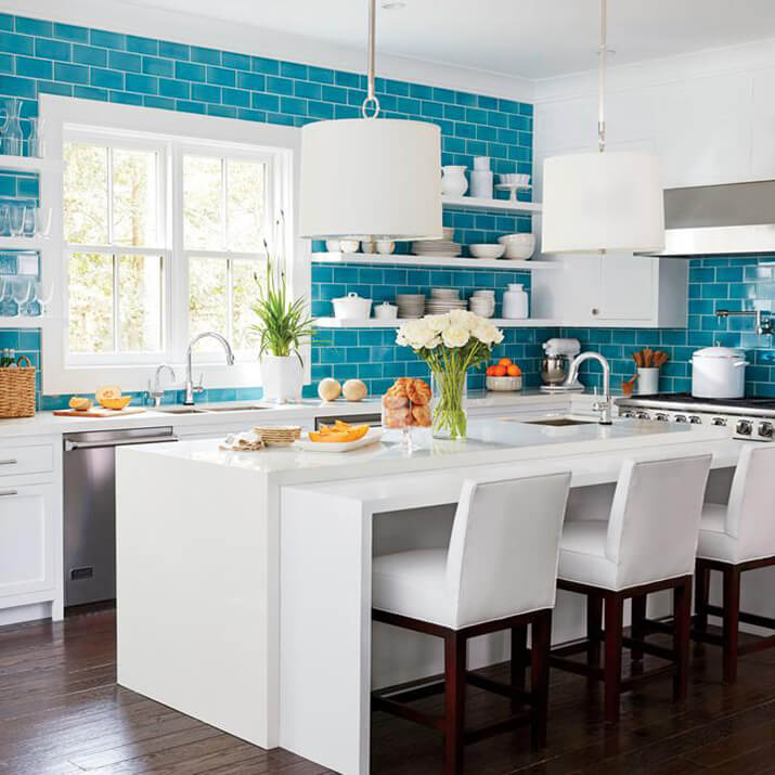 Bright kitchen with white cabinets and blue subway tiles surrounding a window.