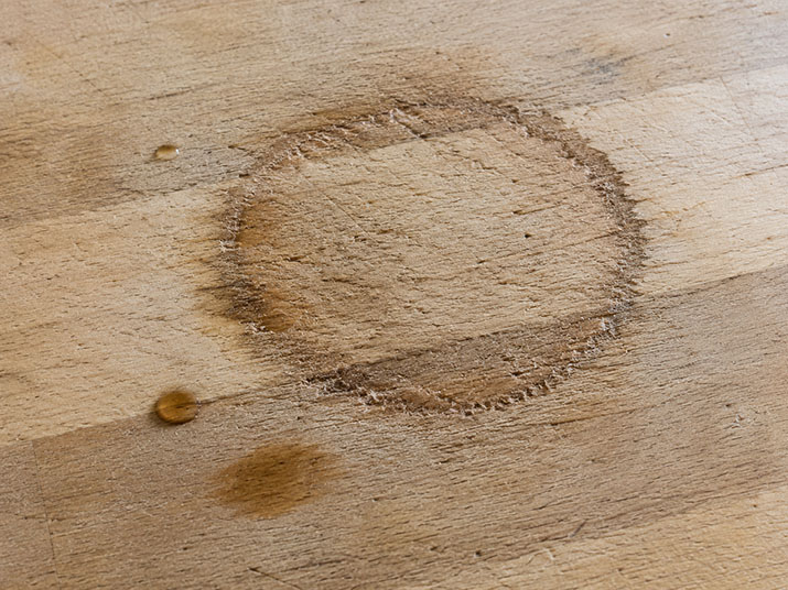 Close-up of water damage on an unsealed butcher block countertop showing dark staining and raised grain around a wet area.