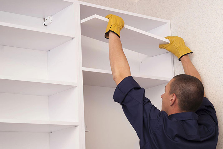 A contractor installing kitchen shelves on the top of cupboards