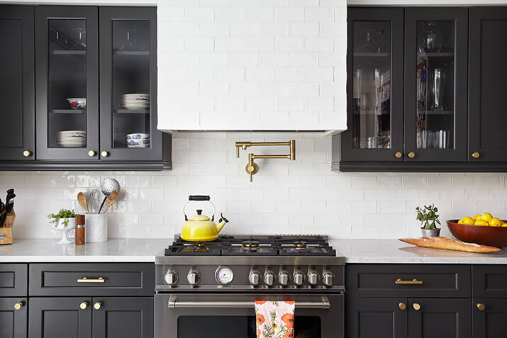 Kitchen with dark cabinets, white backsplash, and gold pot filler.