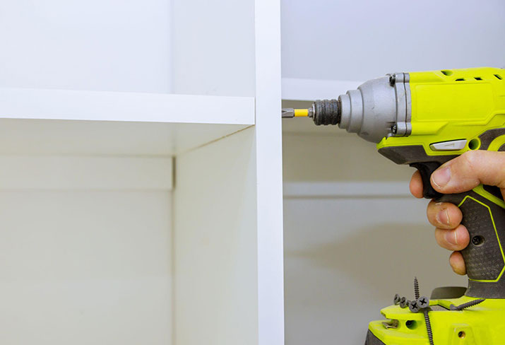 Man with a yellow drill screwing in kitchen shelves.