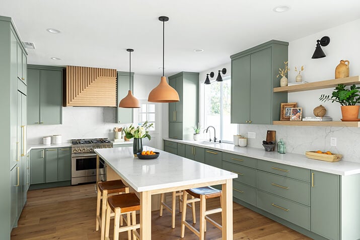 Earthy green cabinets paired with light brown open shelving, range hood, and island.