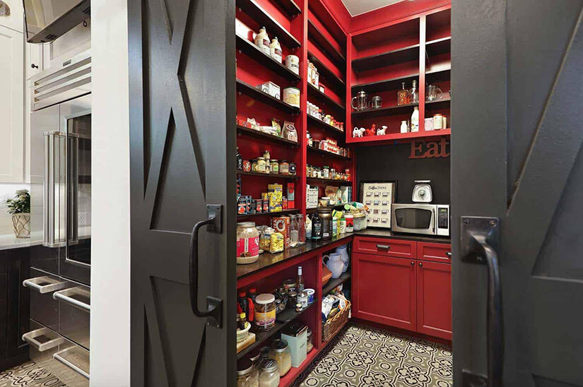 Dark double barn doors open to a farmhouse pantry with red cabinets.