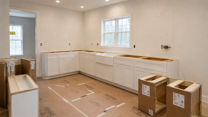 Kitchen mid-remodel with base cabinets installed and upper cabinet spaces empty, showing the installation process.