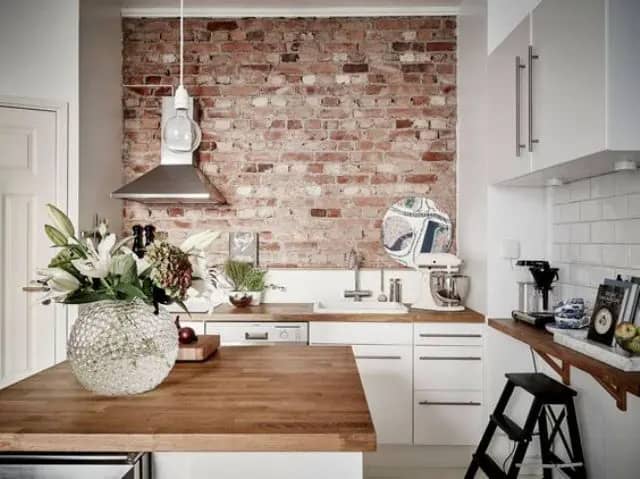 Kitchen with white cabinets, wood countertops, and a brick accent wall.
