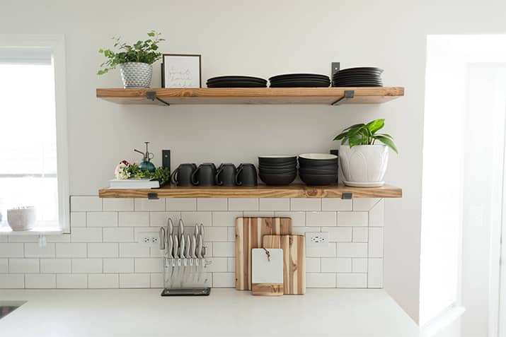 Kitchen with white countertops and wood open shelving and black mugs.
