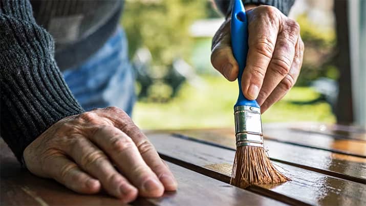 Man applying sealant to a wood table with a paintbrush.