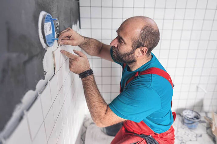 Man installing white tile as shower surround.