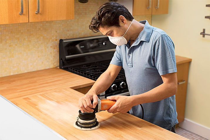 Man using an electric sander to sand kitchen countertops.