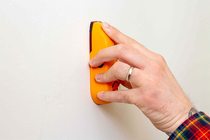 Man using a stud finder on wall.