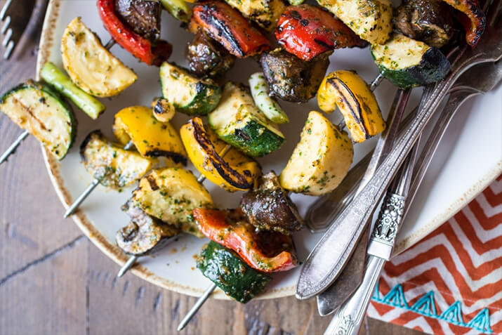 Zucchini, squash, peppers, and mushrooms on metal skewers.