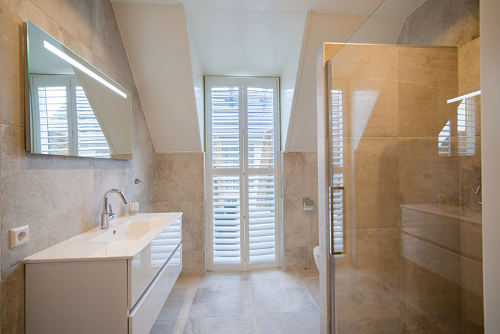 Modern wet room bathroom with stone tile walls, a wall-hung vanity, glass shower partition, and seamless curbless flooring.