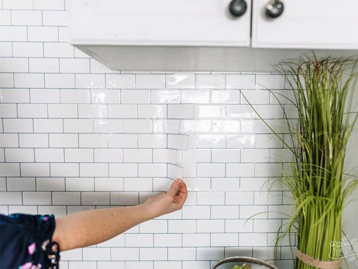 Person applying a white subway tile peel-and-stick kitchen backsplash.