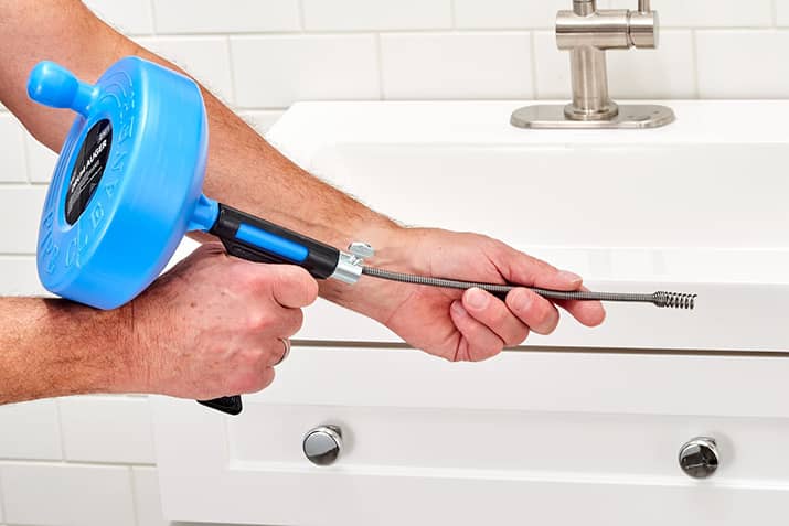 A person holding a handheld plumber's snake in front of a clogged sink.