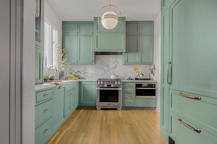 Smoky green mint cabinets paired with gray counters and brass hardware.