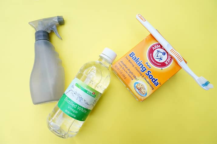 A spray bottle, distilled vinegar, baking soda, and a grout toothbrush.