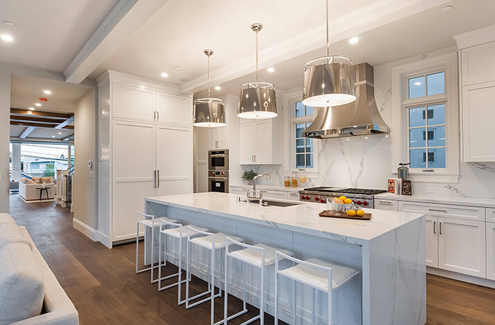 Trendy white kitchen with quartz countertops and solid slab backsplash.