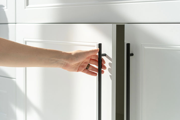 A woman reaching for a cabinet door with fresh modern hardware.