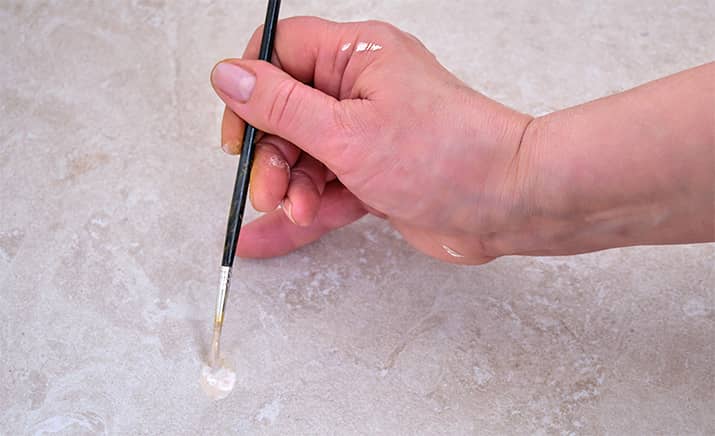 Using a paintbrush to paint and seal a tile repair job.