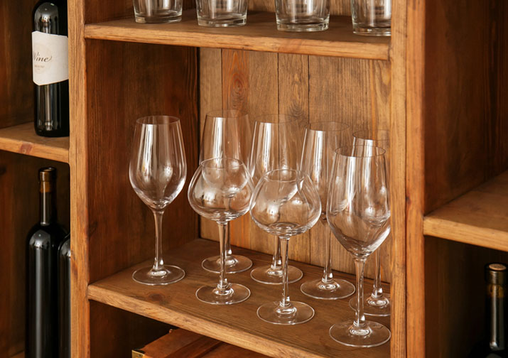 Wine glasses stored on an open shelf above a wine rack.