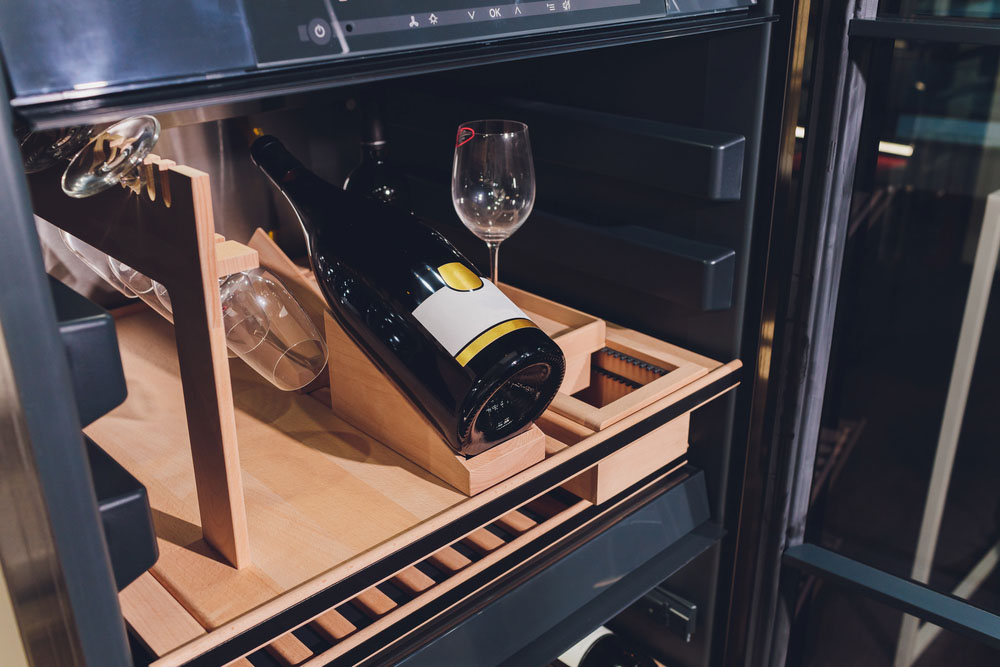 Wine glasses stored upside down on an open shelf above a wine rack.