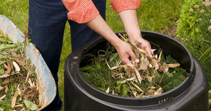 A woman adds leaves and grass clippings to a compost bin.