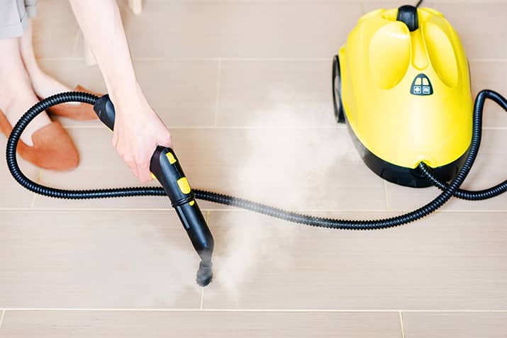 Woman cleaning floor grout with steam cleaner.