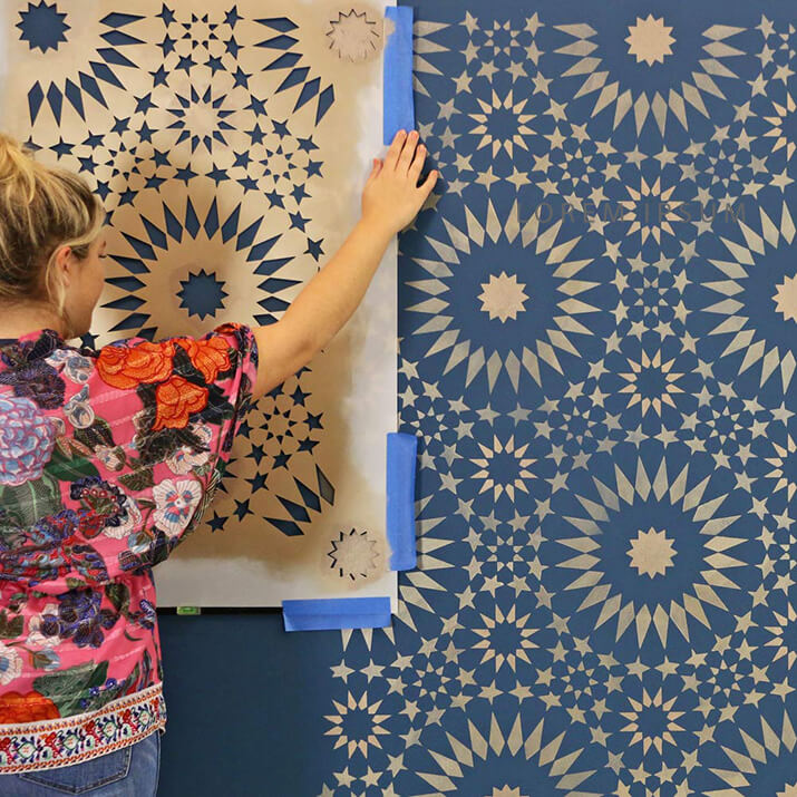 Woman holding up stencil to create a pattern on the wall.