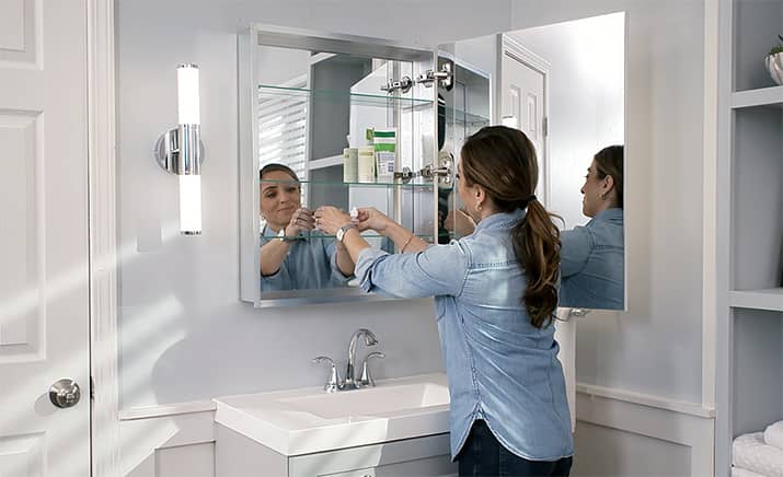 A woman installs a medicine cabinet attached to a mirror surface.