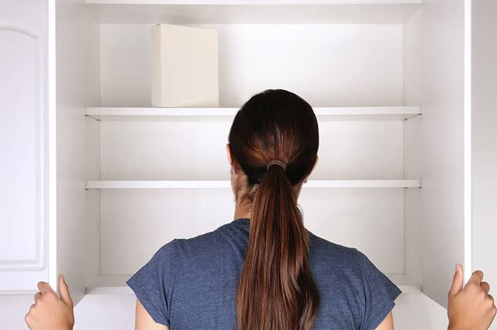 Woman opening cabinet to an empty pantry.
