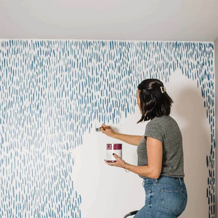 Woman painting dynamic brush stokes in blue on wall.