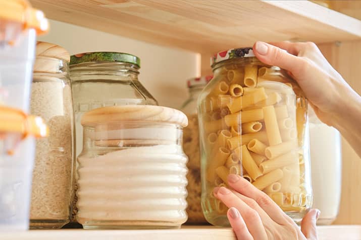 Woman restocking kitchen pantry with pasta in glass jars.