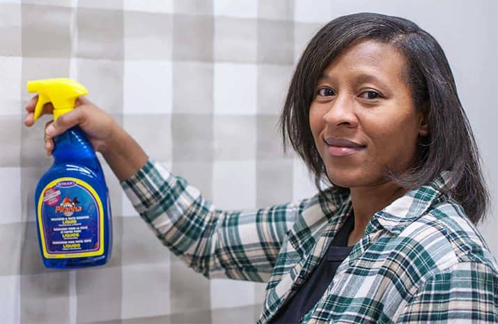 Person spraying wallpaper removal solution onto wallpaper.