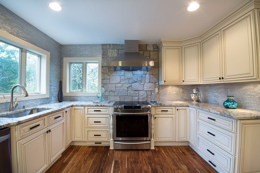 Pearl glazed cream cabinets in a kitchen with a stone accent wall and a stainless range