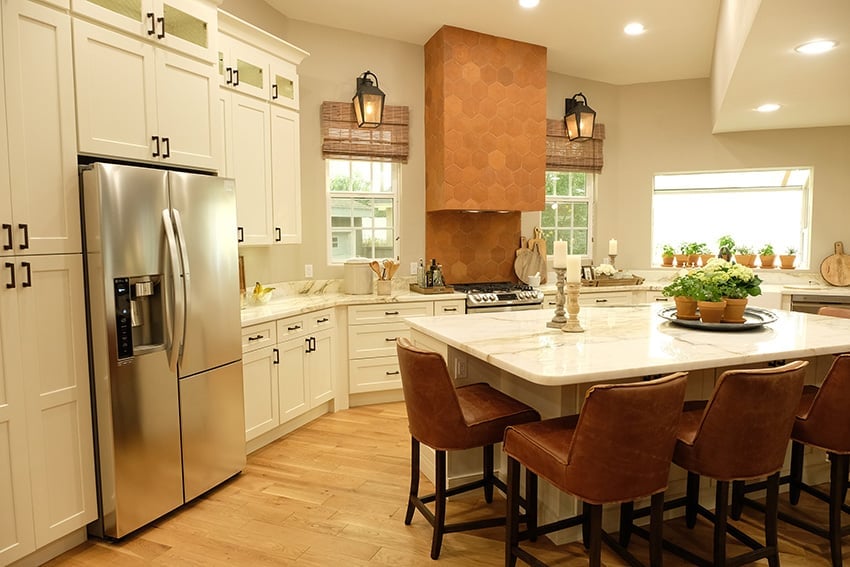 Shaker Antique White cabinets with a copper range hood and leather stools