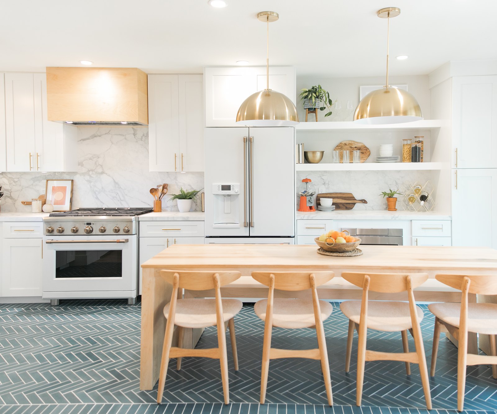 A white shaker kitchen with brass pendants, a wood island table and a teal tile floor