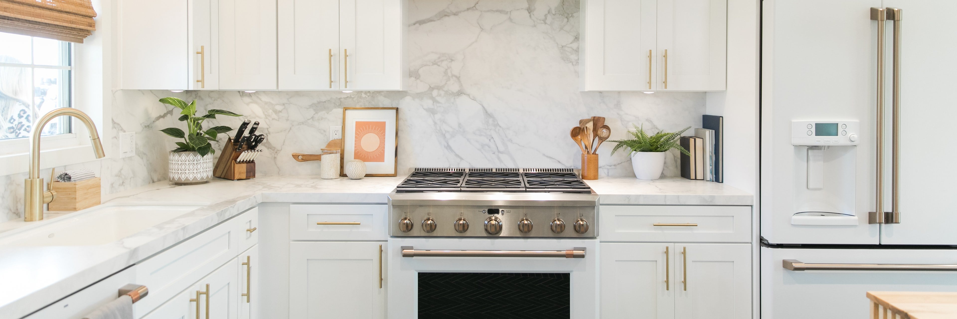 A white shaker kitchen with a marble backsplash and brass hardware
