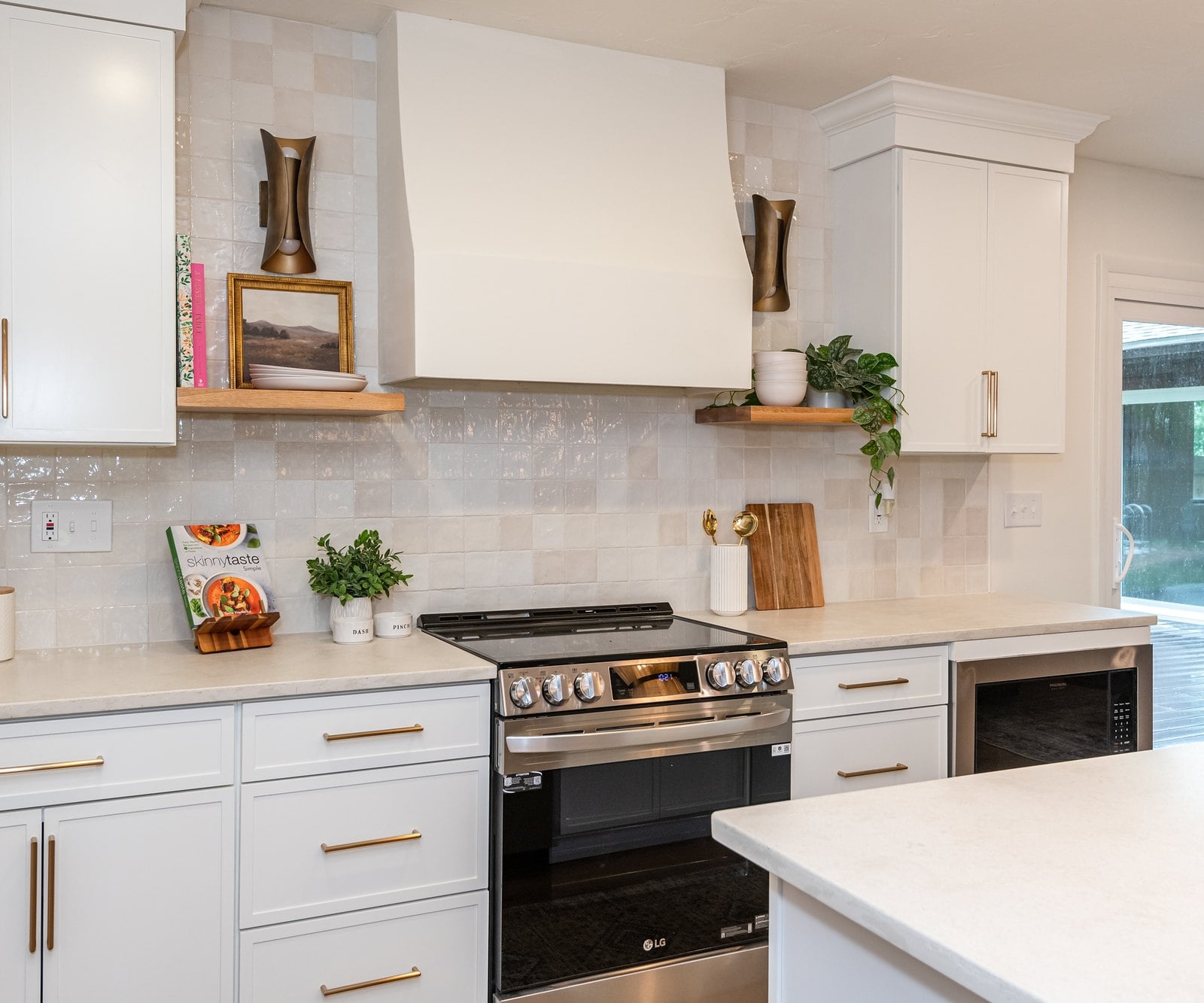 A white kitchen with a plaster range hood, a handmade tile backsplash and brass pulls