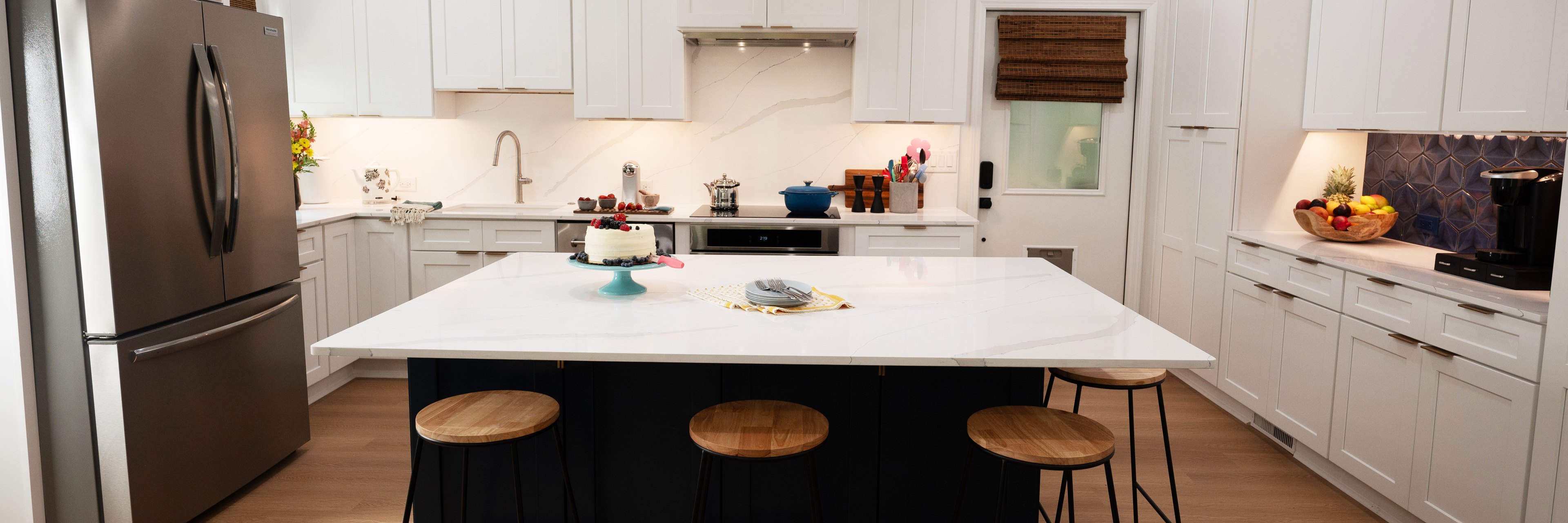 A white shaker kitchen with a navy blue island, a quartz counter and wood stools