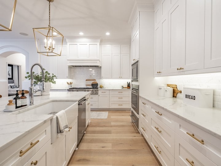 A white shaker kitchen with brass hardware, a farmhouse sink and a long run of drawers