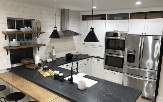 A finished white shaker kitchen with open shelving and a dark stone counter