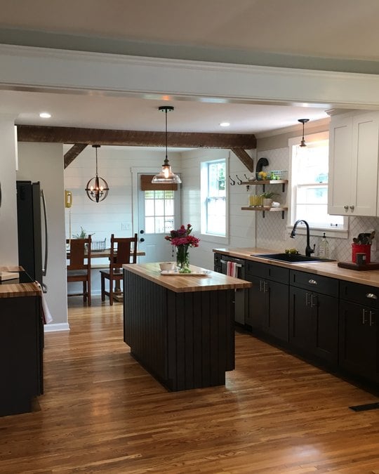 A kitchen with a black island, butcher block counters and white shaker uppers