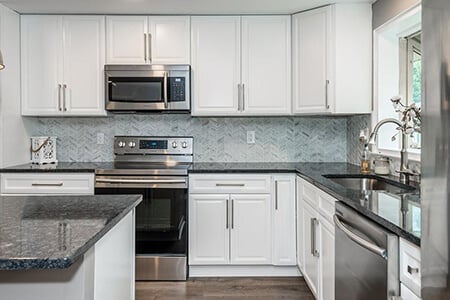 White shaker cabinets with silver pulls and tile backsplash in modern kitchen.