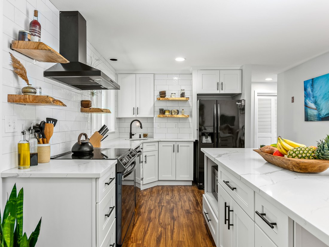 An Ice White Shaker kitchen with floating wood shelves and a black range hood
